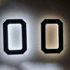 A pair of modern, black, rectangular LED house numbers with automatic dusk-to-dawn lighting mounted on a white wall.