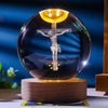 A dark glass crystal ball night light featuring a glowing crucifix silhouette against a dark background.