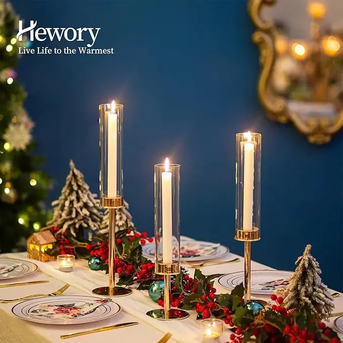 Three hurricane candle holders with gold and silver accents decorated with red berries on a white table.