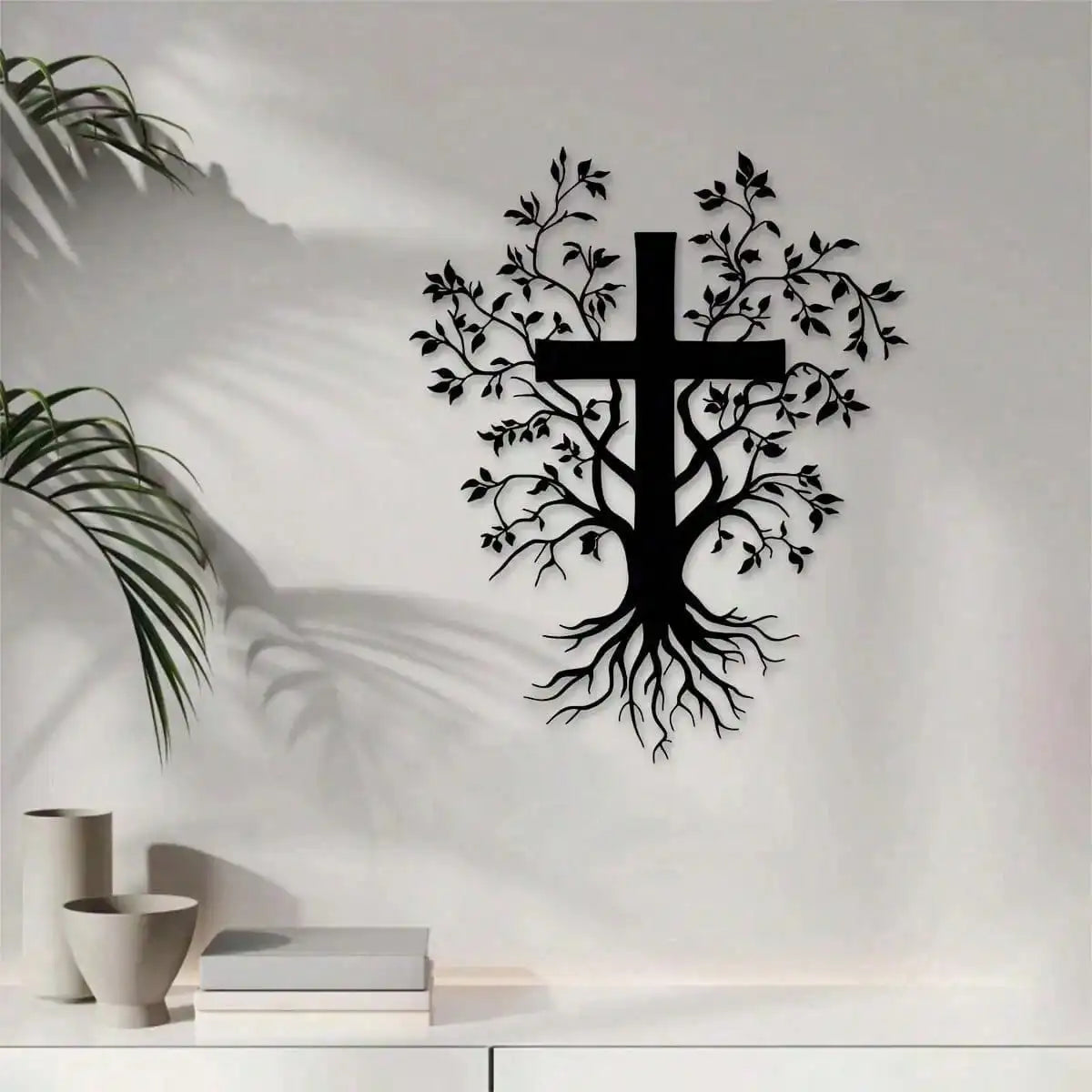 Black silhouette of a cross with leafy branches and roots on a white wall.