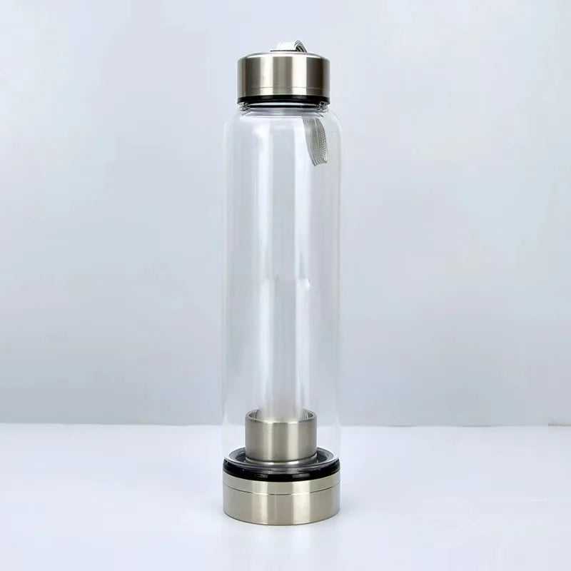 Botella de agua de vidrio transparente con tapa y base metálica, usada para curación cristalina natural.