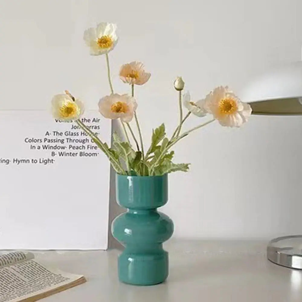 A glass flower vase holds several delicate, light-colored flowers on a white surface.