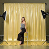 A woman in a black sequin top and pants poses in front of a shimmering gold sequin backdrop curtain for photography.