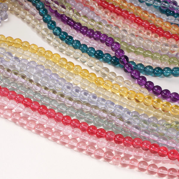 A collection of round glass spacer beads in various colors like purple, green, yellow, and pink are displayed on a white surf