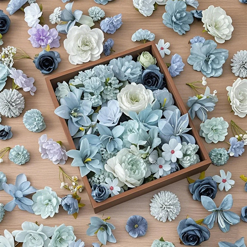 A collection of mini silk artificial flower heads in various shades of blue, gray, and white arranged in a wooden box.