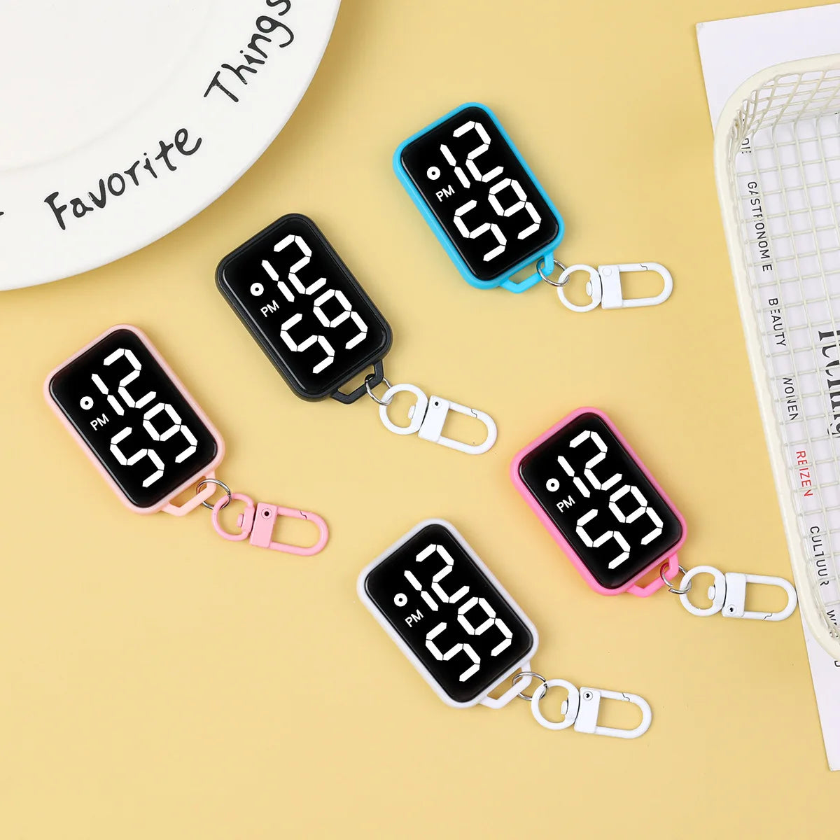 A collection of LED keychain pocket watches with digital displays in black, pink, and blue colors displayed on a light backgr