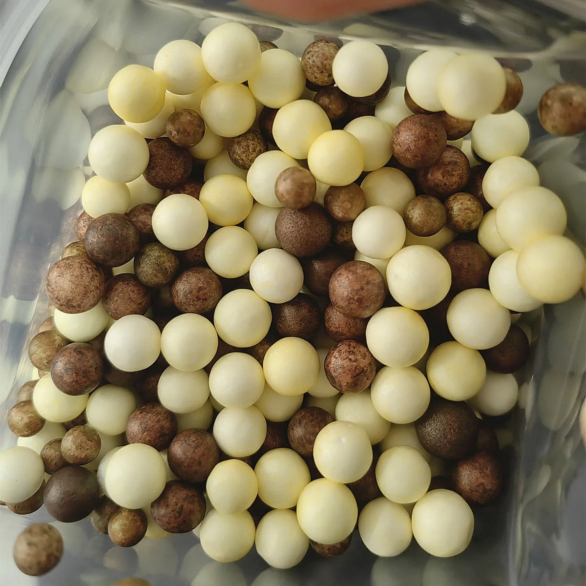 A collection of pastel foam beads in various shades including white, cream, and brown are displayed in a clear container.