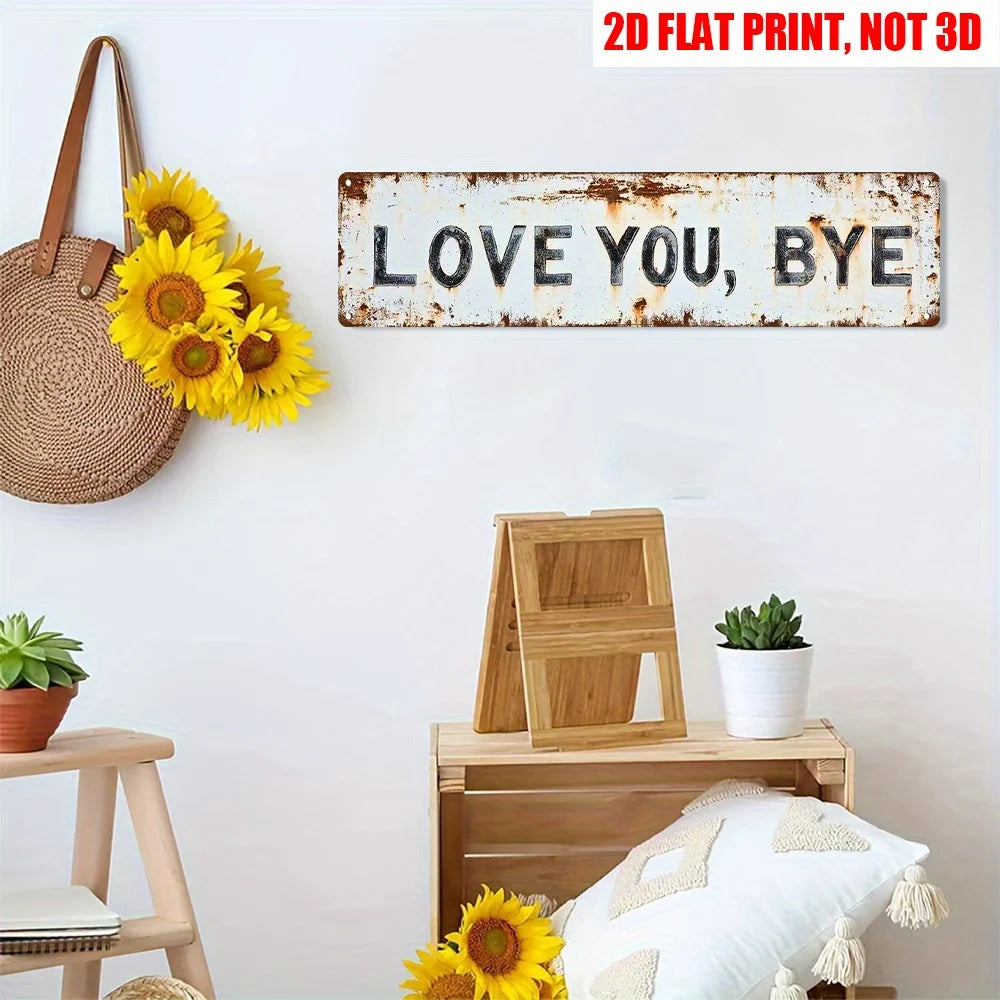 A rustic metal sign with the text LOVE YOU BYE mounted on a white wall, surrounded by potted plants and wooden furniture.