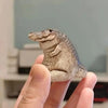 A hand holds a small, textured resin crocodile tea pet ornament against a light background.