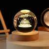 A glowing crystal ball night light with a silhouette of a cake inside, resting on a wooden base.