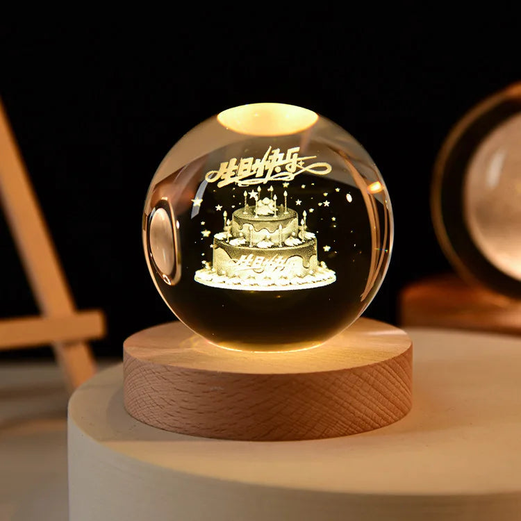 A glowing crystal ball night light with a silhouette of a cake inside, resting on a wooden base.