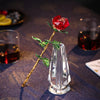 Handcrafted crystal glass rose vase with a red rose and golden leaves on a dark blue fabric.