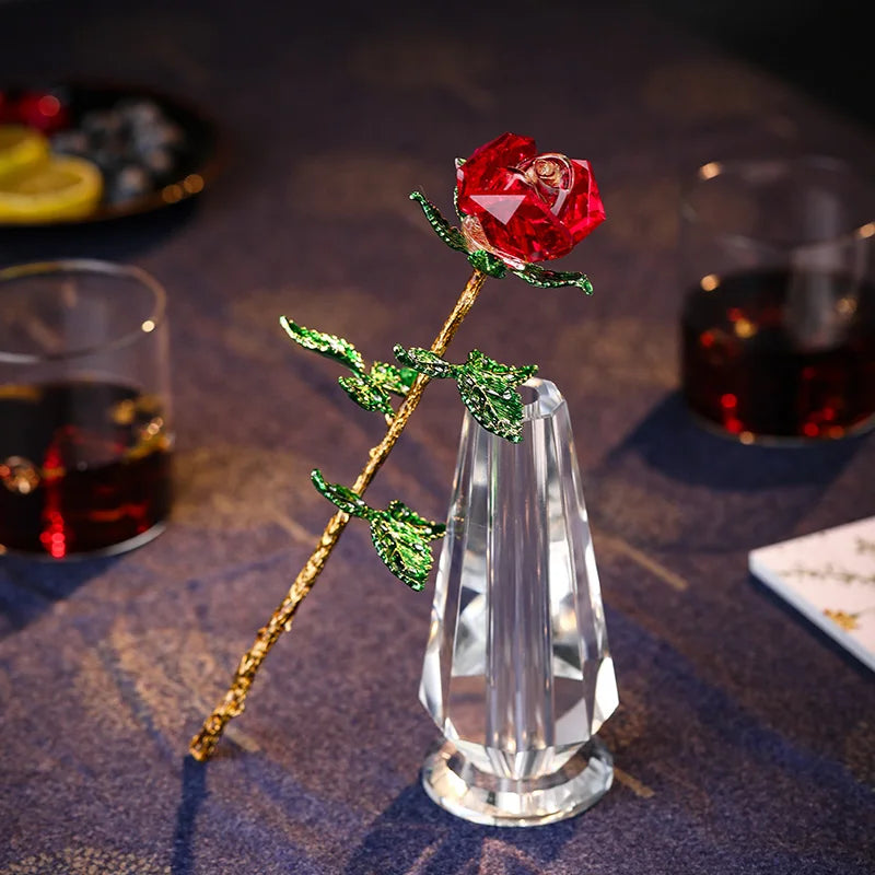 Handcrafted crystal glass rose vase with a red rose and golden leaves on a dark blue fabric.