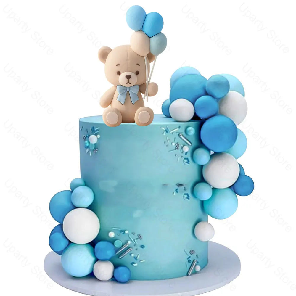 A light blue cake decorated with blue and white foam balloon toppers and a teddy bear topper.