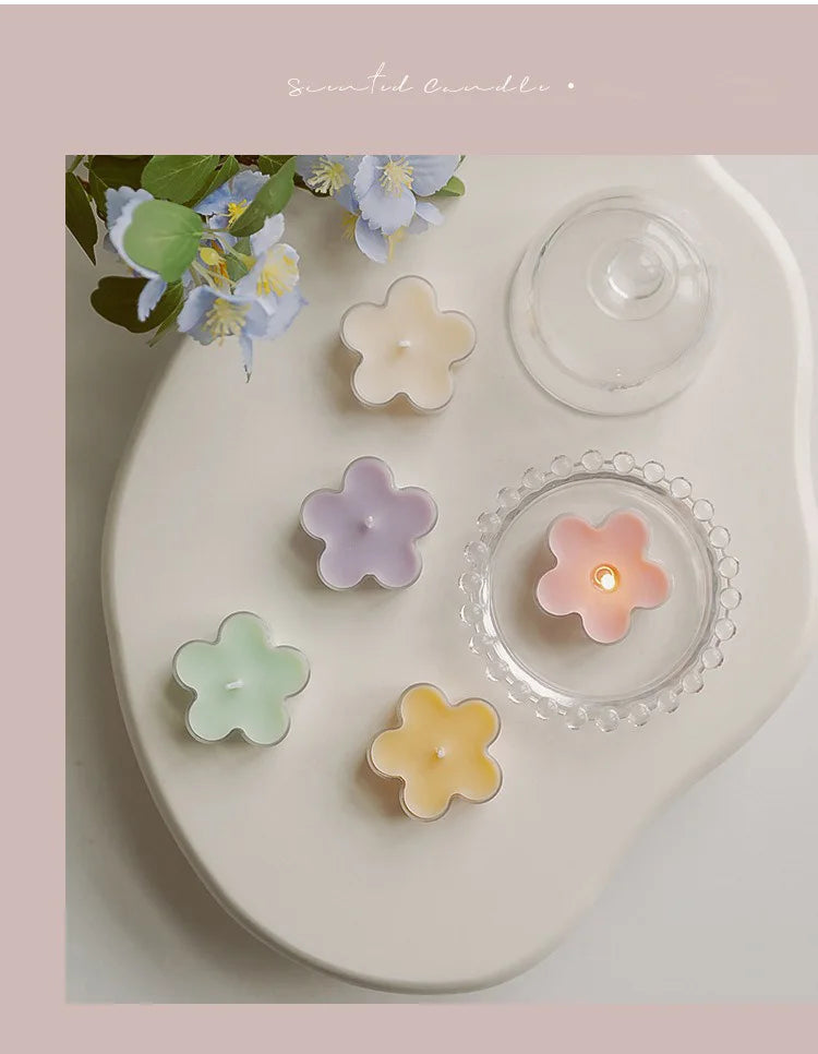 A white ceramic plate displays a handmade soy wax flower tea light candle in various pastel colors and a glass lid.