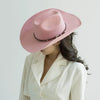 A woman wearing a pink felt cowboy hat with a studded leather band and a cream blazer.