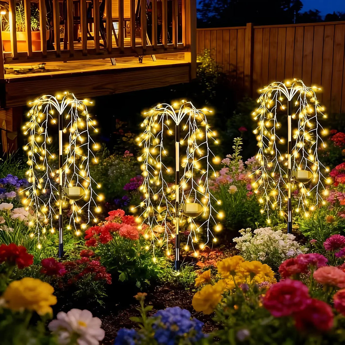 Three vertical solar garden lights with bright yellow LED fireworks starburst effects illuminating colorful flowers.