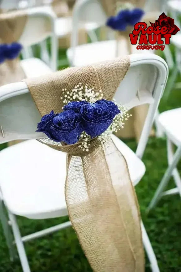 A close-up of a white chair decorated with a burlap ribbon tied around the back, featuring a dark blue artificial rose.