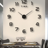 A modern black wall clock with silver hands and numbers on a white wall above a dining table.