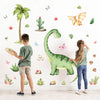 A young boy and girl are decorating a white wall with large green dinosaur stickers.