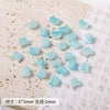 A collection of light blue cat head glass beads for jewelry making scattered on a white surface.