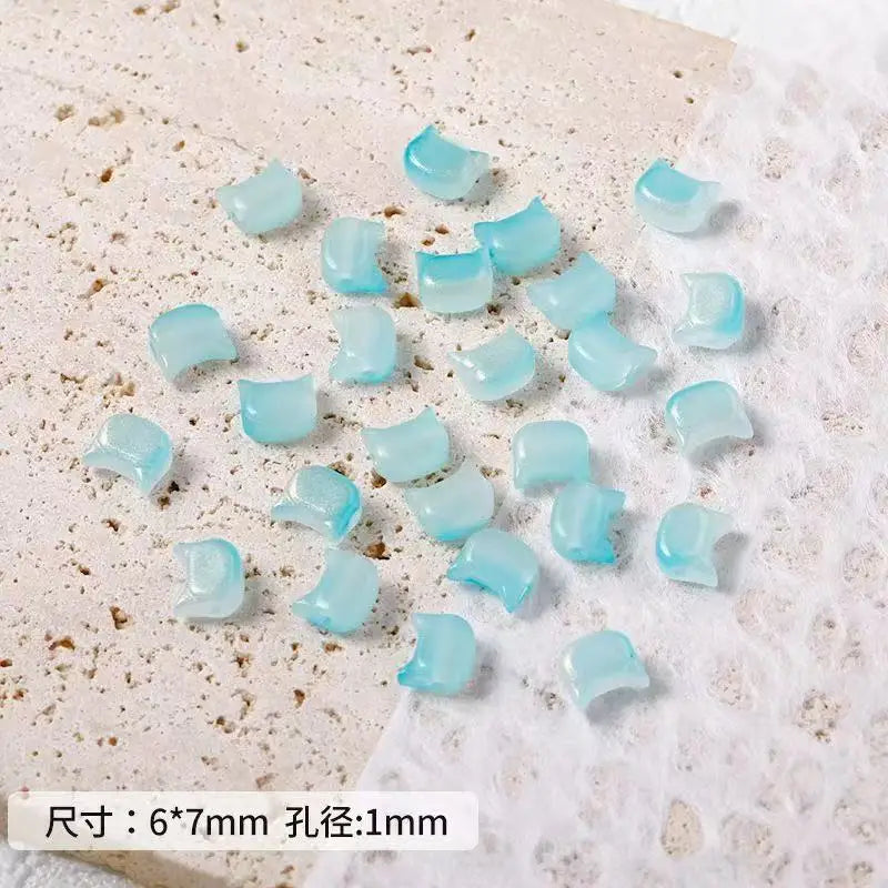 A collection of light blue cat head glass beads for jewelry making scattered on a white surface.