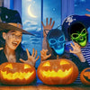 A woman wearing a witch hat smiles while holding an LED glow skull mask and carved pumpkins.