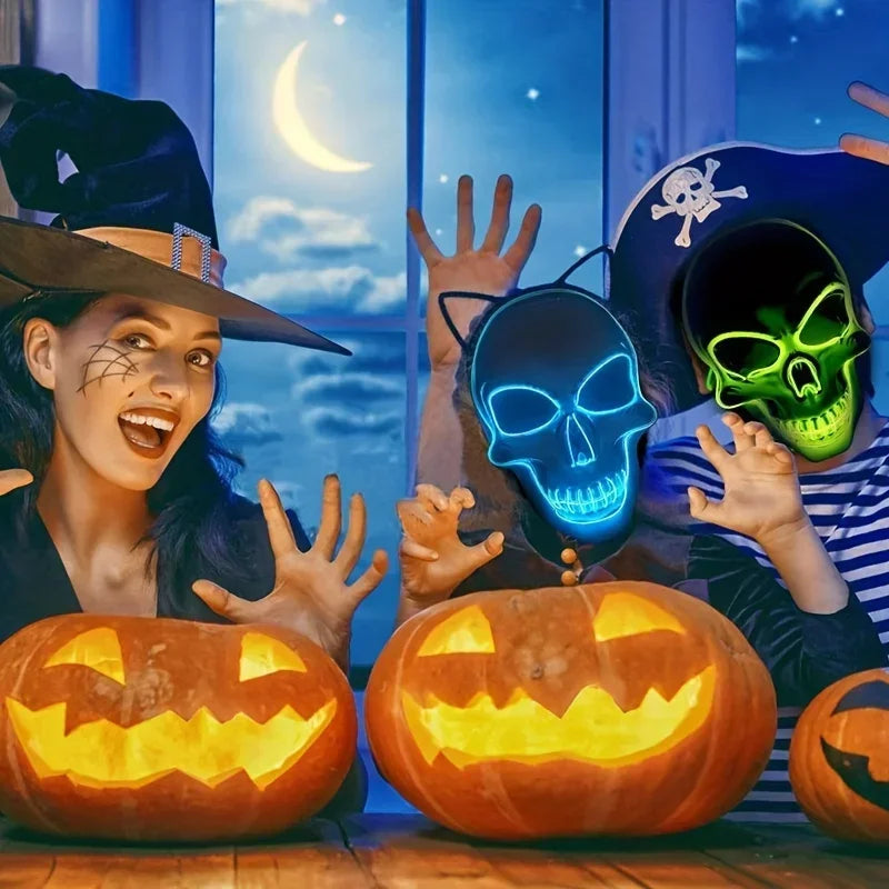 A woman wearing a witch hat smiles while holding an LED glow skull mask and carved pumpkins.