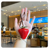A hand holds a red strawberry charm and keychain in a cafe setting.