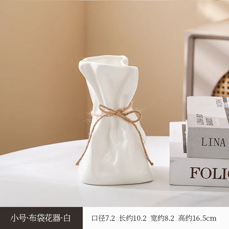 White ceramic money bag shaped vase with twine detail on a white surface.