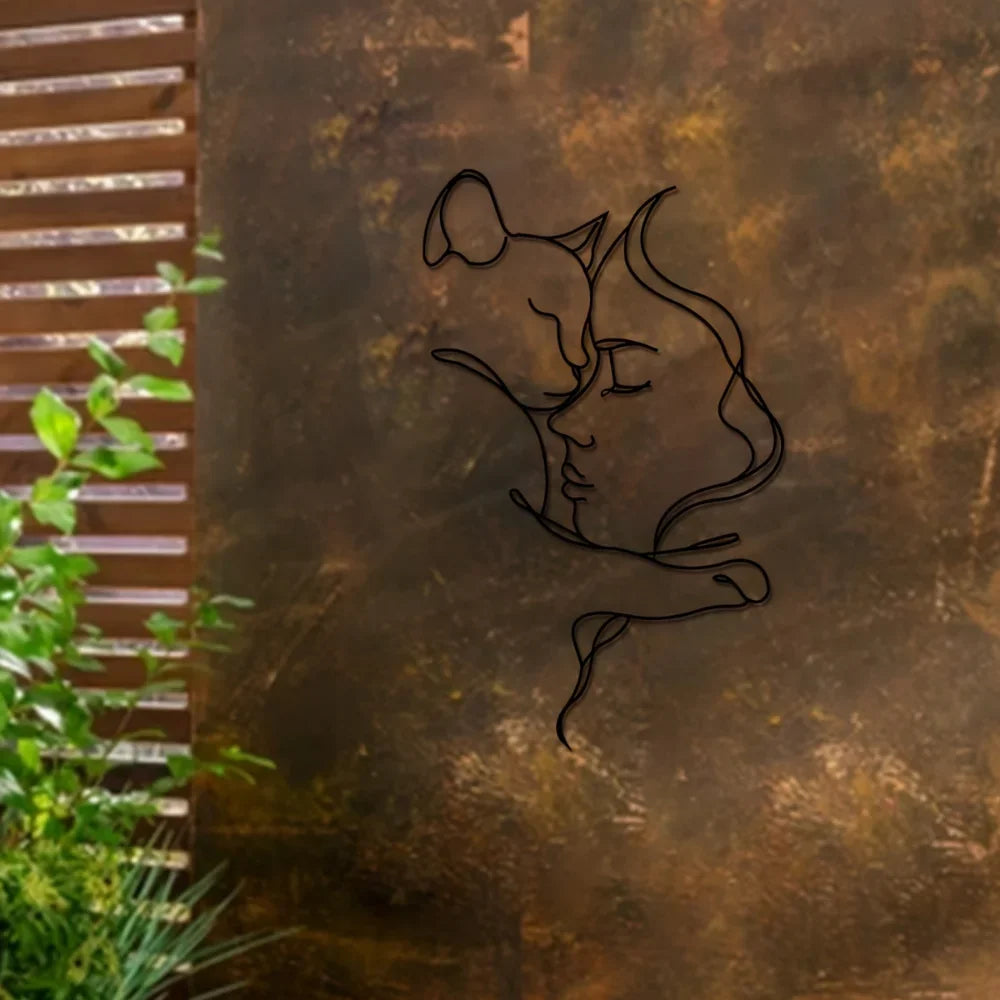 A black silhouette of a woman embracing a cat is etched onto a textured, bronze-colored metal surface.