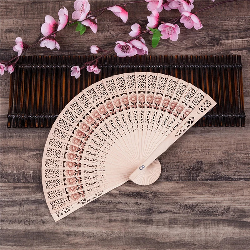 Hand carved bamboo folding fan with pink flowers resting on a wooden surface.