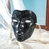 A black ancient style masquerade mask with intricate detailing is displayed on a white cloth.