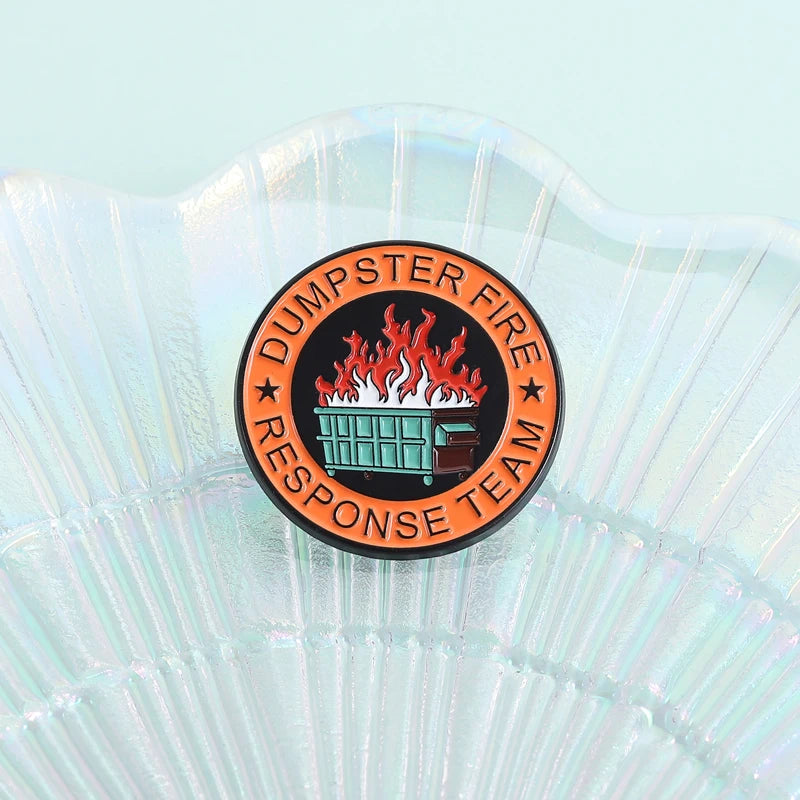 An enamel pin featuring a stylized orange and black design with flames and text for the Dumpster Fire Response Team.