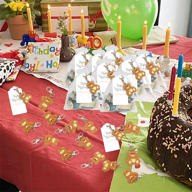 A display of cute bear keychain party favors with organza bags and thank you tags arranged on a red tablecloth.