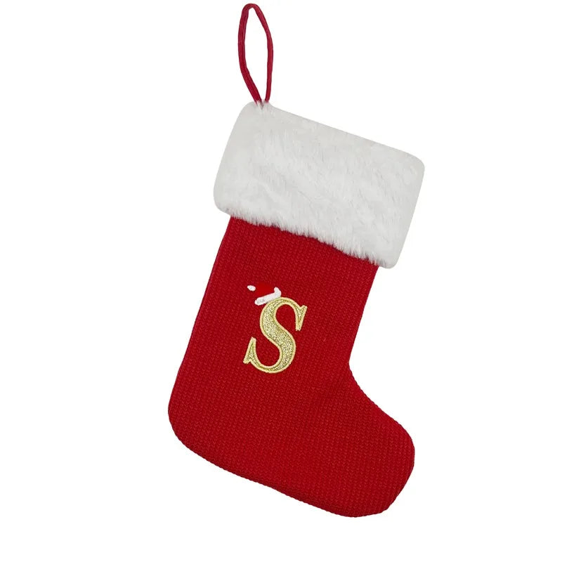 A red knitted Christmas stocking with a white fluffy cuff and a gold letter S decoration.