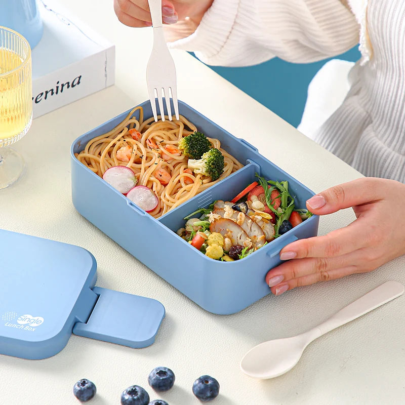 A blue bento lunch box filled with pasta and vegetables, next to a fork and spoon.