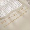 Gold ultra-thin layering chain bracelets displayed on a light background next to a white wavy dish.