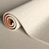 A roll of beige artificial grass carpet for outdoor decor, showing the texture and rolled form.