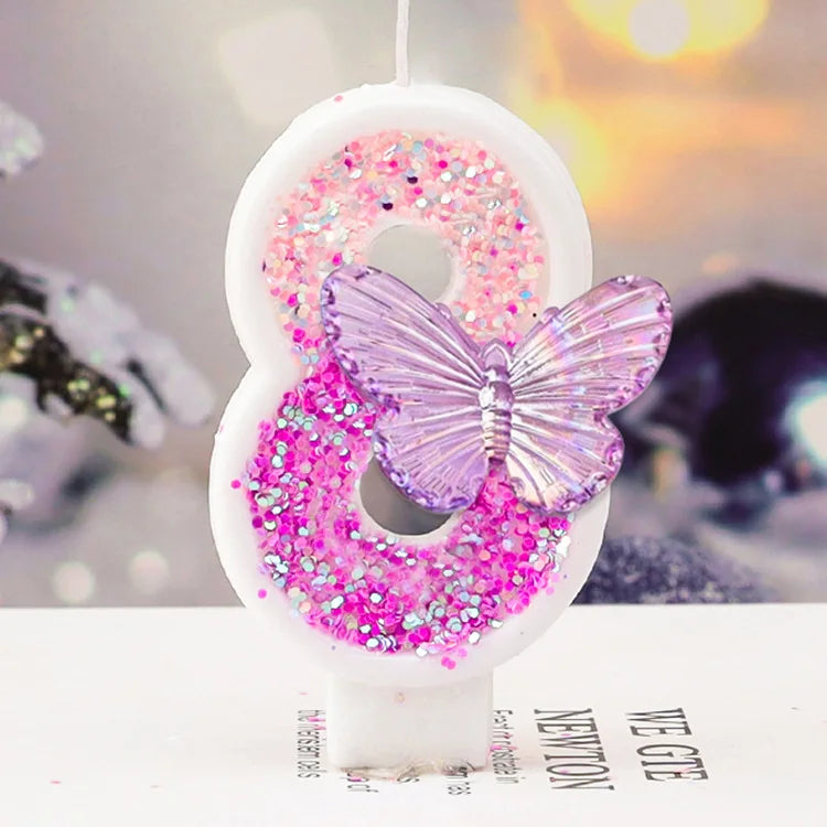 A white birthday candle shaped like the number 8 decorated with pink and purple glitter and a butterfly detail.