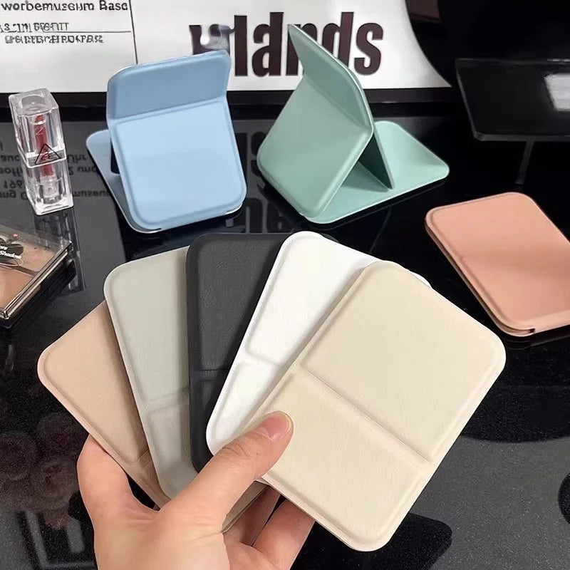 A hand holds a portable folding HD makeup mirror with various pastel colored cases and a stand.