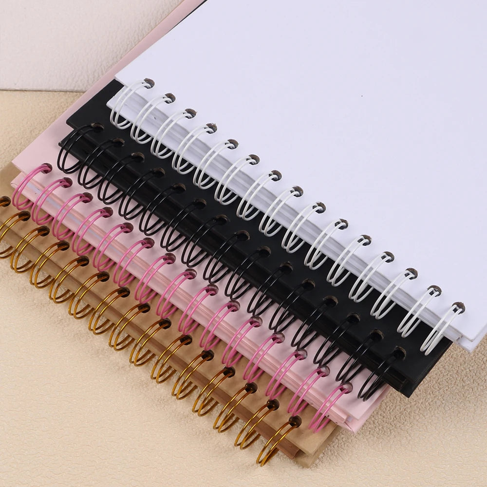 A stack of spiral-bound kraft paper scrapbooks in various colors including black, pink, and gold.