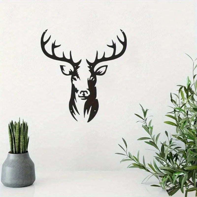 Black metal deer head wall sculpture against a white background with green foliage.