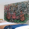 A close-up of an urban graffiti tapestry featuring bold, colorful street art writing on a gray background.