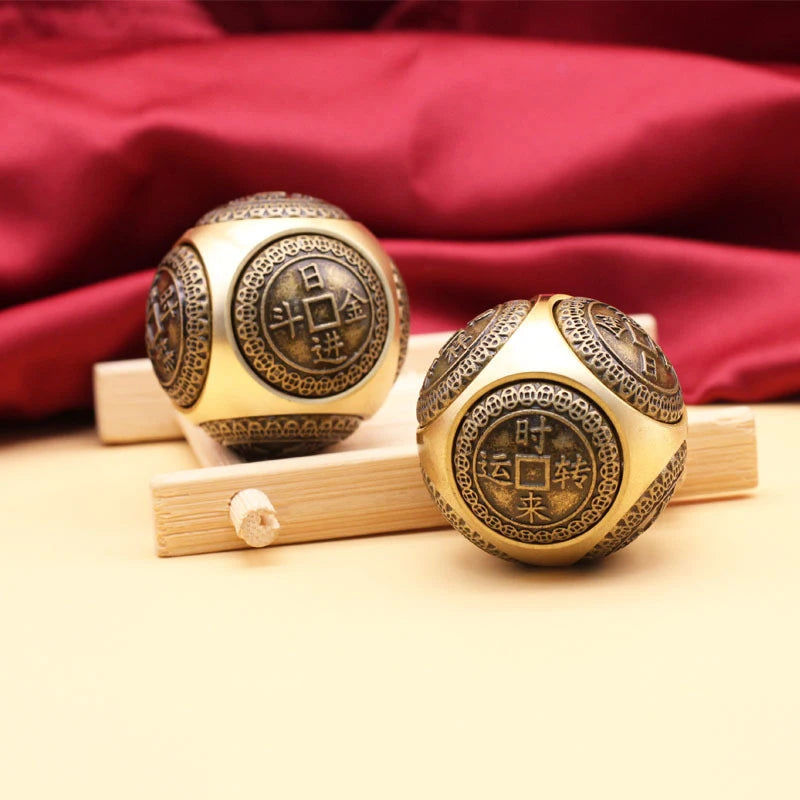 A pair of gold-colored Chinese lucky coin spinners resting on a light wooden surface against a deep red fabric background.