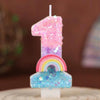 A birthday candle shaped like the number one made of pink and purple glitter with a rainbow and blue cloud base
