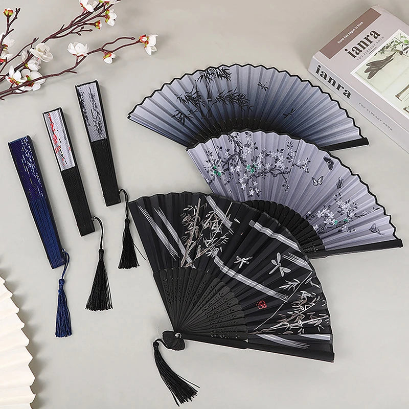 A collection of elegant vintage Chinese folding hand fans in various shades of gray and black, displayed on a light surface.