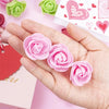 Una mano sostiene varias decoraciones de rosas artificiales rosas sobre un fondo rosa claro.