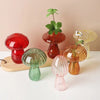 A collection of mushroom-shaped glass vases in translucent red, green, and amber colors displayed on a white surface.