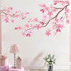 Pink peach blossom branch wall decals featuring pink flowers on a white wall with a small house and floral arrangement.